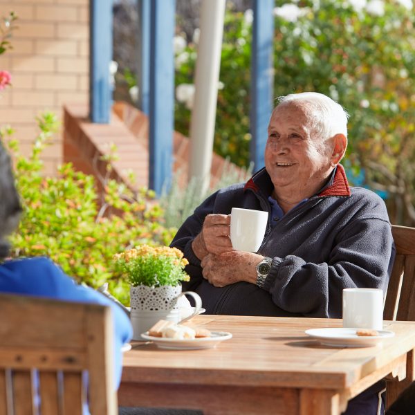Resident smiling while enjoying a cup of coffee in the garden at St Margaret's Community Retirement Village
