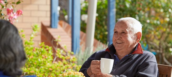 Man smiling and enjoying a cup of tea while sitting outside