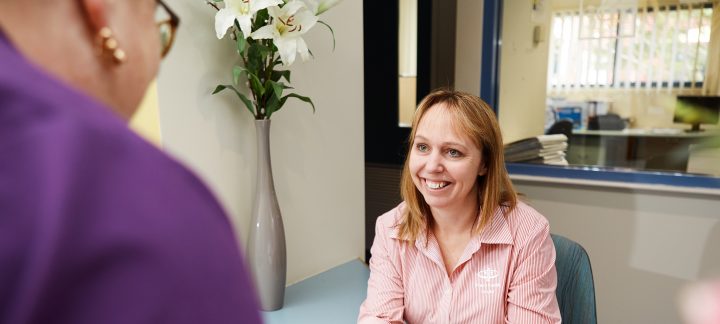 Close-up of a resident talking to a staff member sitting at a reception desk