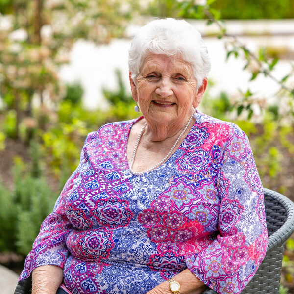 A female resident sitting out in the garden at Mercy Place Colac smiling wearing a purple top