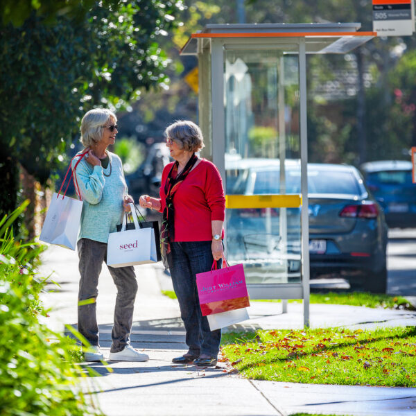 Two women with shopping bags having a chat at the bus stop near St Margaret's Retirement Village