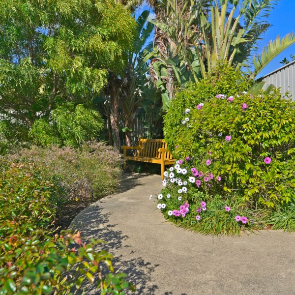 Lush green garden and walkway with pink and white flowers at St Margaret's Community Retirement Village