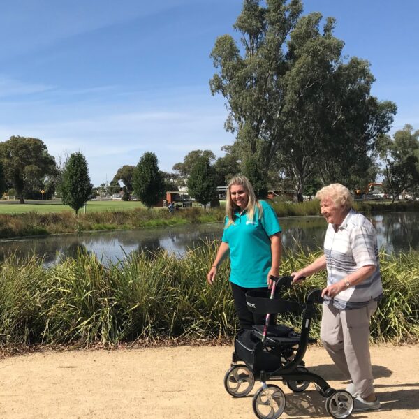 Home care client with walking aid enjoying a leisurely stroll around Shepparton lake with her home care worker